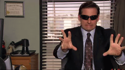 A Man In A Suit And Tie Wearing Sunglasses Is Sitting In Front Of A Window GIF