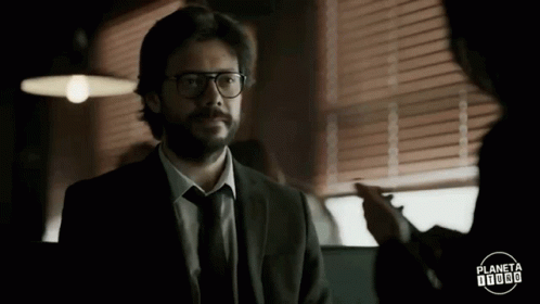 A Man In A Suit And Tie With Glasses Is Talking To Another Man . GIF