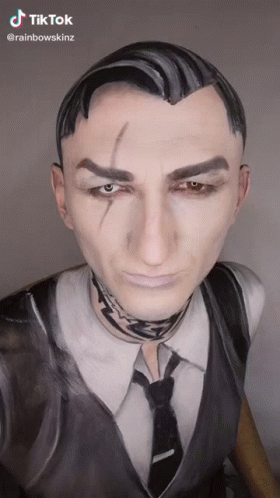 A Man In A Suit And Tie With His Face Painted . GIF