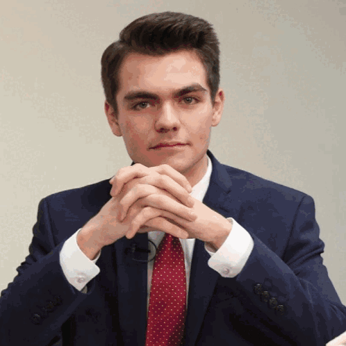 A Man In A Suit And Tie With His Hands Folded In Front Of His Face GIF