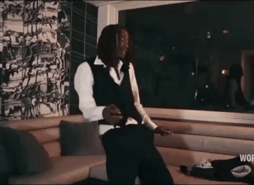 A Man In A Suit And Vest Is Standing In A Living Room Smoking A Cigarette . GIF