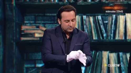 a man in a suit and white gloves stands in front of a wall of books