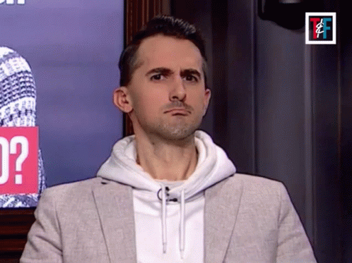 A Man In A Suit And White Hoodie Is Making A Funny Face GIF