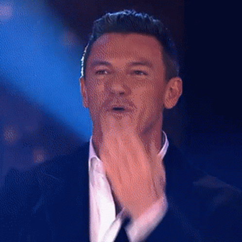 A Man In A Suit And White Shirt Is Clapping His Hands On A Stage . GIF