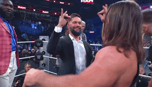 A Man In A Suit And White Shirt Is Giving A High Five To Another Man In A Wrestling Ring . GIF