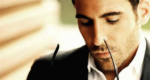 A Man In A Suit And White Shirt Is Holding A Pair Of Glasses In His Mouth . GIF
