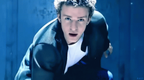 A Man In A Suit And White Shirt Is Kneeling Down In Front Of A Blue Wall . GIF