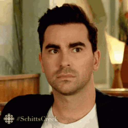 A Man In A Suit And White Shirt Is Making A Funny Face While Sitting In A Chair . GIF