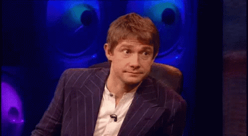 A Man In A Suit And White Shirt Is Sitting In A Chair In Front Of A Microphone . GIF