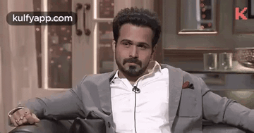 A Man In A Suit And White Shirt Is Sitting In A Chair With His Hands On His Knees . GIF