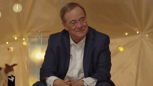 Man In Suit Sitting In Front Of A Sign GIF