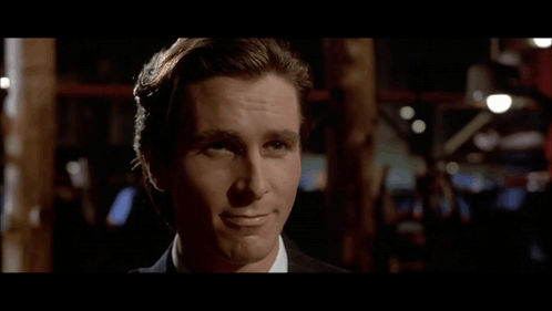 A Man In A Suit And White Shirt Is Smiling And Looking At The Camera GIF