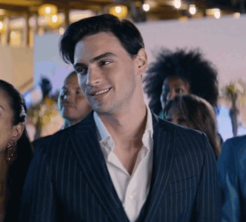 A Man In A Suit And White Shirt Is Smiling In A Crowd GIF