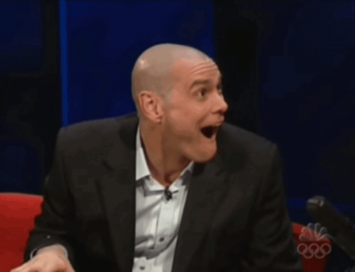 A Man In A Suit And White Shirt Is Smiling In Front Of A Nbc Logo GIF