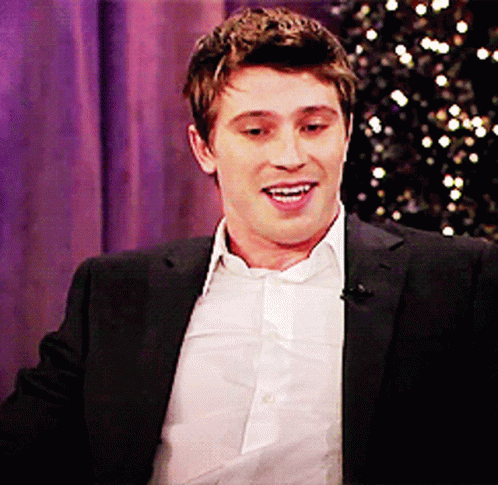 A Man In A Suit And White Shirt Is Smiling In Front Of A Purple Curtain GIF