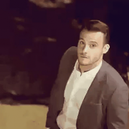 a man in a suit and white shirt is standing in a dark room looking at the camera .