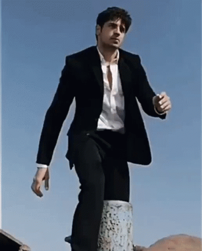 A Man In A Suit And White Shirt Is Standing On A Post GIF