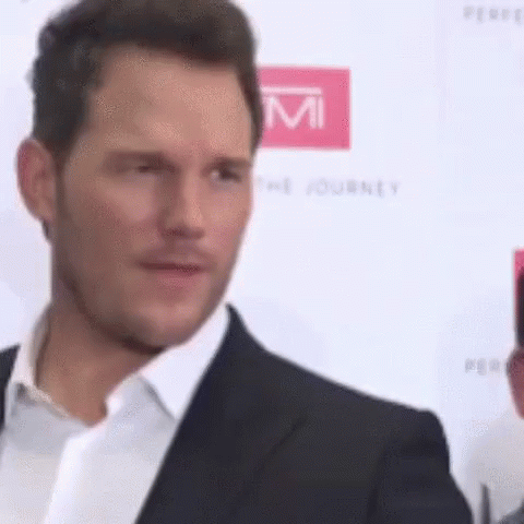 A Man In A Suit And White Shirt Is Standing On A Red Carpet And Looking At The Camera . GIF