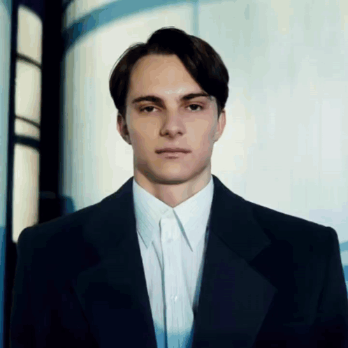 A Man In A Suit And White Shirt Stands In Front Of A Window GIF
