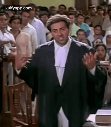 A Man In A Suit And Wig Is Standing In Front Of A Crowd In A Courtroom . GIF