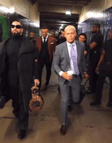 A Man In A Suit Carrying A Boxing Ring Is Walking Down A Hallway GIF