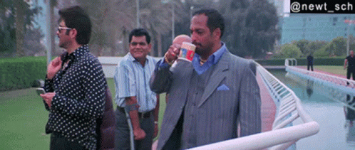 A Man In A Suit Drinking From A Cup That Says ' Noodles ' On It GIF