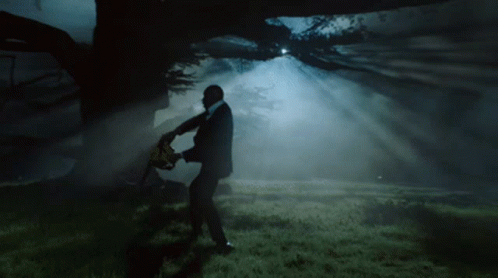 A Man In A Suit Holding A Chainsaw In A Dark Forest GIF