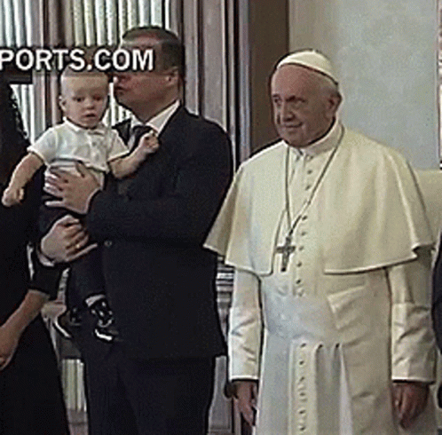 A Man In A Suit Holds A Baby In Front Of A Man In A White Robe With The Words Ports.com On The Bottom Right GIF