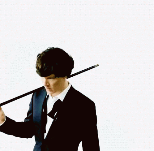 A Man In A Suit Holds A Cane Over His Shoulder GIF