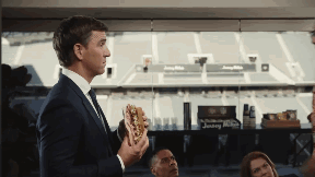 a man in a suit holds a hot dog in front of a stadium