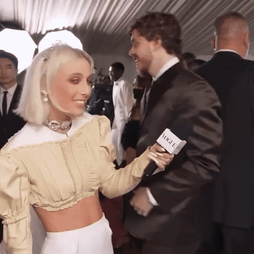 A Man In A Suit Holds A Microphone That Says Vogue On It GIF