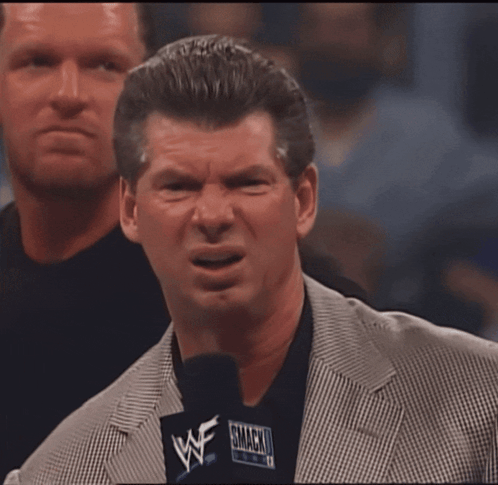 A Man In A Suit Holds A Microphone That Says Wwe On It GIF