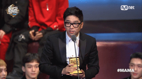 A Man In A Suit Holds A Trophy In Front Of A Microphone At A Music Awards GIF