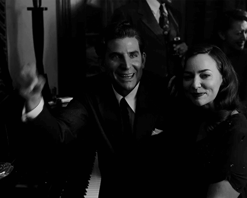 A Man In A Suit Holds Up A Cigar Next To A Woman GIF
