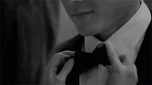 A Man In A Suit Is Adjusting His Bow Tie In A Black And White Photo GIF