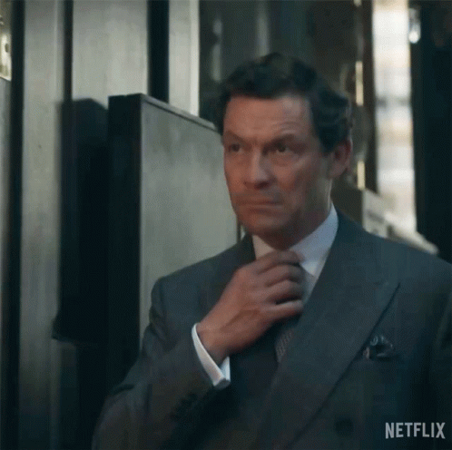 A Man In A Suit Is Adjusting His Tie In A Hallway . GIF