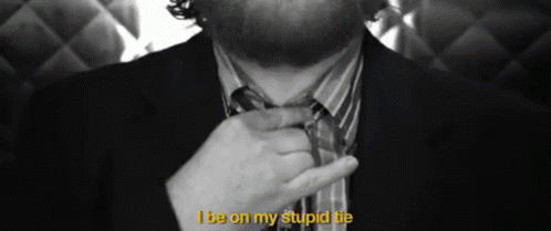 A Man In A Suit Is Adjusting His Tie With The Words I Be On My Stupid Tie Above Him GIF