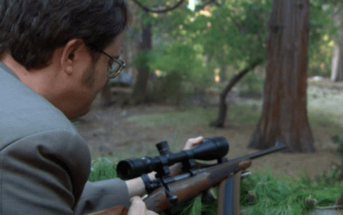 A Man In A Suit Is Aiming A Rifle With A Scope GIF