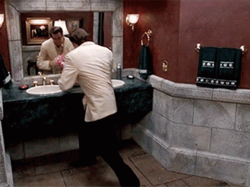 A Man In A Suit Is Brushing His Teeth In Front Of A Bathroom Mirror GIF