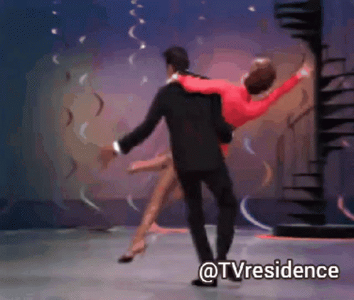 A Man In A Suit Is Carrying A Woman In A Red Dress On A Stage With The Words @Tvresidence Below Them GIF
