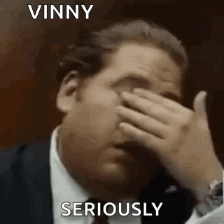 A Man In A Suit Is Covering His Face With His Hand And Says Vinny Seriously . GIF
