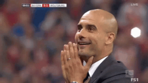 A Man In A Suit Is Covering His Face With His Hands While Watching A Soccer Game Between Bayern And Wolfsburg . GIF