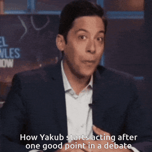 A Man In A Suit Is Covering His Mouth With His Hand While Talking About Yakub GIF