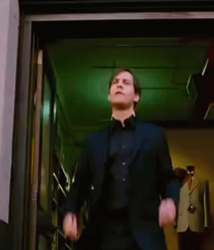 A Man In A Suit Is Dancing In A Doorway While A Woman Stands Behind Him . GIF