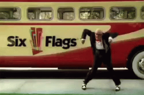A Man In A Suit Is Dancing In Front Of A Bus That Says Six Flags . GIF