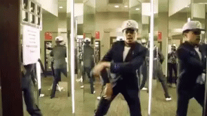 A Man In A Suit Is Dancing In Front Of A Mirror While Wearing A Hat With The Letter S On It GIF
