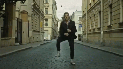 A Man In A Suit Is Dancing In The Middle Of A Cobblestone Street GIF