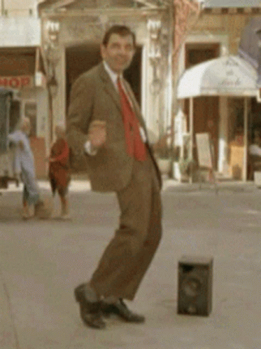 A Man In A Suit Is Dancing On A Sidewalk In Front Of A Store That Says Mop GIF