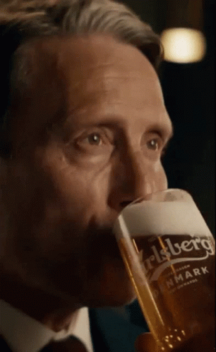 A Man In A Suit Is Drinking From A Carlsberg Glass GIF