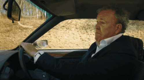 A Man In A Suit Is Driving A Car And Looking At His Watch GIF